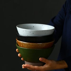 Handmade ramen bowl in black, white, and green glaze finishes on a wooden table.