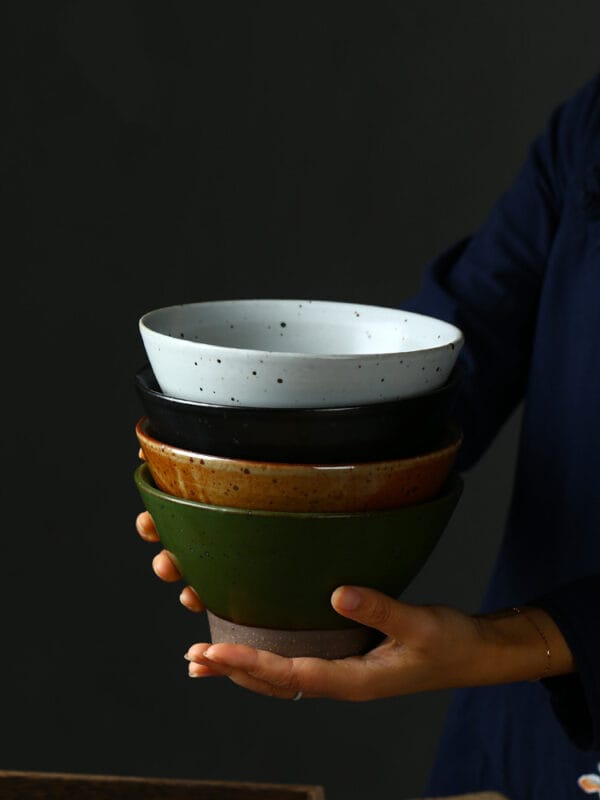 Handmade ramen bowl in black, white, and green glaze finishes on a wooden table.